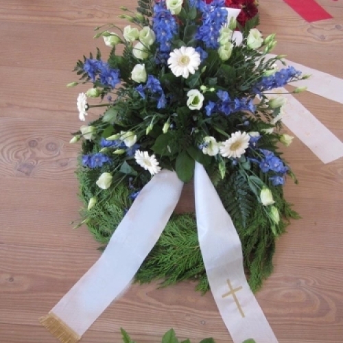 Begravelseskrans med blå blomster og hvide detaljer med bånd