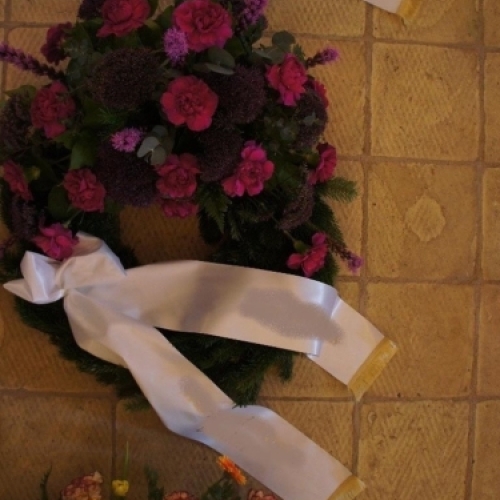 Begravelseskrans med mørkelilla blomster og grønt med bånd