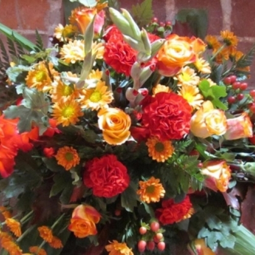 Bårebuket med røde og orange blomster samt grønne detaljer