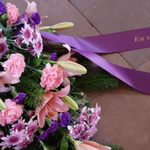 Bårebuket med lyserøde blomster og lilla bånd med teksten En sidste hilsen