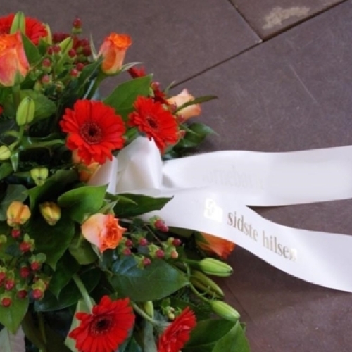 Bårebuket med røde gerbera, orange roser og bånd med teksten En sidste hilsen