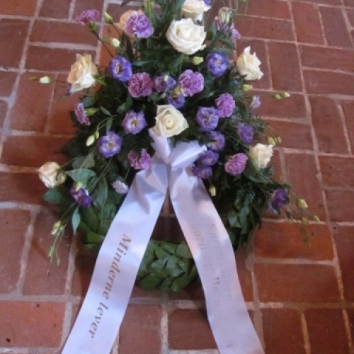 Begravelseskrans med pink gerbera og grøn bund med hvidt bånd