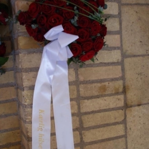 Begravelseskrans med røde roser og hvidt bånd med tekst