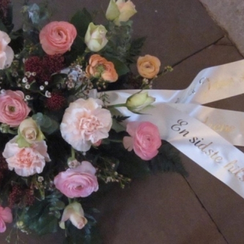 Begravelseskrans i rosa nuancer med blomster og hvidt bånd