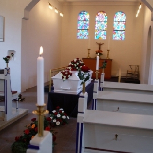 Kirkerum pyntet til begravelse med kiste, blomsterdekorationer og lys