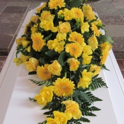 Kistepynt med solsikker og grønt løv på hvid kiste