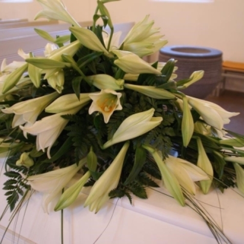 Kistepynt med orange blomster og hvidt mindebånd på kiste