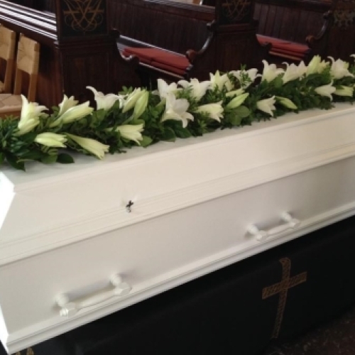 Kistepynt med røde roser og hvide blomster lagt på hvid kiste