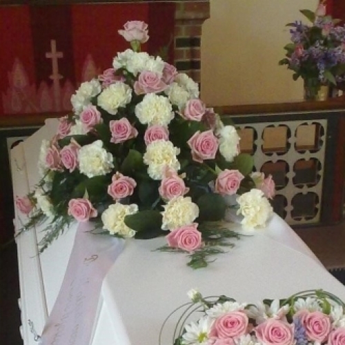 Kistepynt med lyserøde roser og hvide nelliker arrangeret på hvid kiste til begravelse