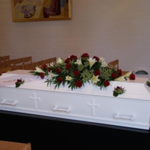 Klassisk kistepynt med røde og hvide roser arrangeret på hvid kiste