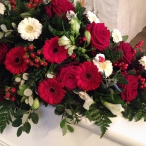 Lang kistepynt med hvide liljer og grønt løv på hvid kiste