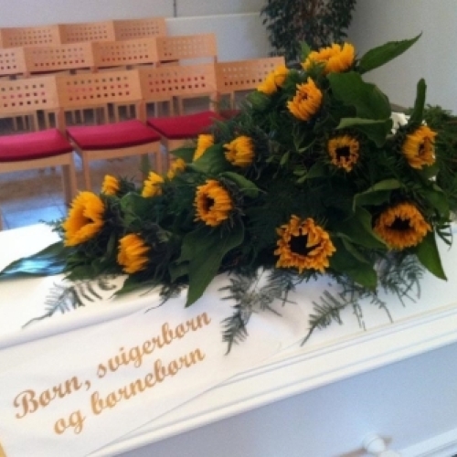 Kistepynt med solsikker og grønt løv på hvid kiste