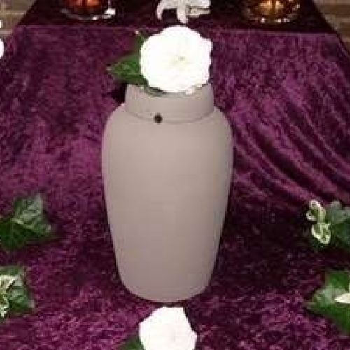 Urneopstilling med lilla drapering og blomster omkring urnen