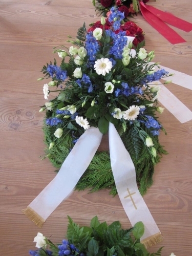 Begravelseskrans med blå blomster og hvide detaljer med bånd