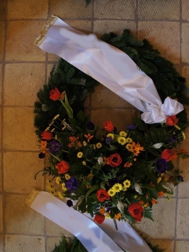 Begravelseskrans med farverige blomster og gran med bånd