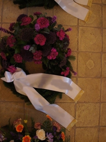 Begravelseskrans med mørkelilla blomster og grønt med bånd