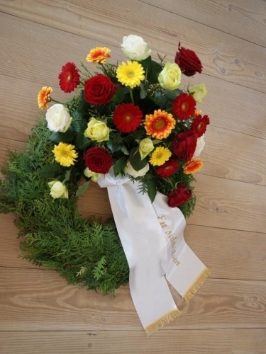 Begravelseskrans med farverige blomster og gran med bånd