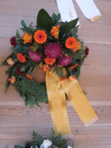 Begravelseskrans med orange og lilla blomster med gult bånd