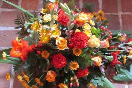 Bårebuket med røde og orange blomster samt grønne detaljer