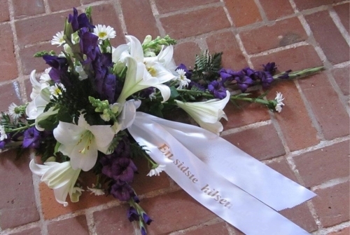 Bårebuket med hvide liljer, lilla blomster og bånd med tekst