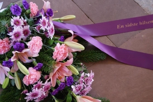 Bårebuket med lyserøde blomster og lilla bånd med teksten En sidste hilsen