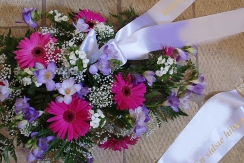 Bårebuket med pink gerbera, lilla blomster og hvidt bånd