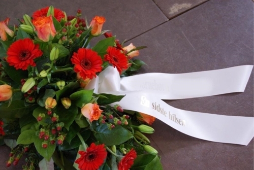 Bårebuket med røde gerbera, orange roser og bånd med teksten En sidste hilsen