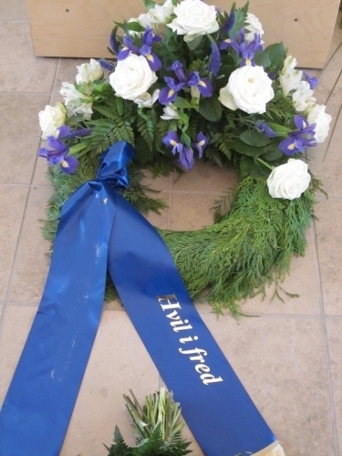 Begravelseskrans med orange liljer og røde blomster med hvidt bånd