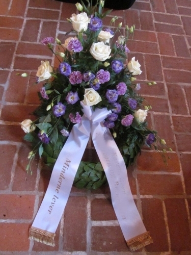 Begravelseskrans med pink gerbera og grøn bund med hvidt bånd