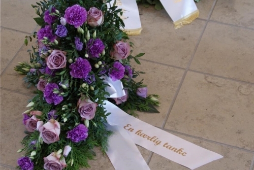 Begravelseskrans med lilla roser, lilla blomster og hvidt bånd