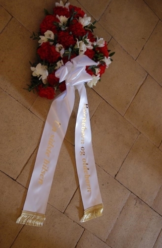 Begravelseskrans med røde og hvide blomster og hvidt bånd