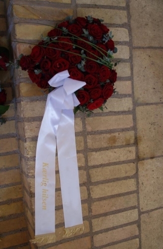 Begravelseskrans med røde roser og hvidt bånd med tekst