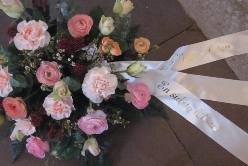 Begravelseskrans i rosa nuancer med blomster og hvidt bånd
