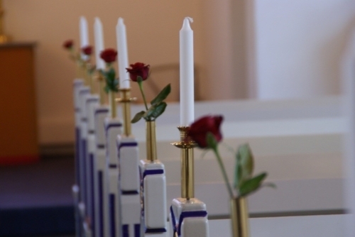 Kirkepynt med hvide lys og røde roser langs kirkebænkene