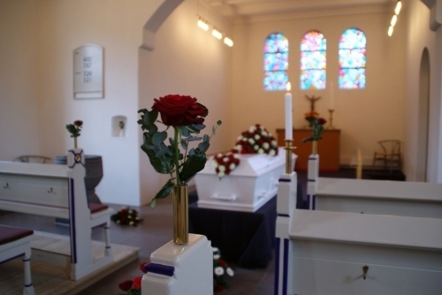 Kirkepynt med rød rose i vase og lys ved kiste i kirken