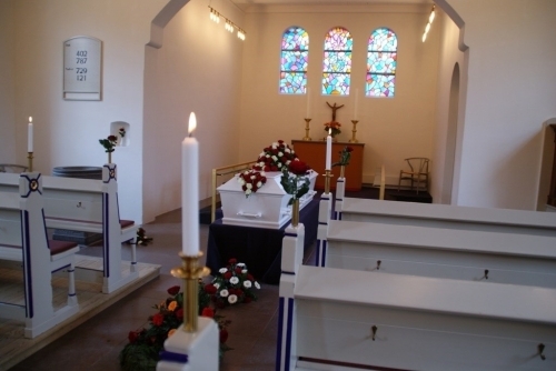 Kirkerum pyntet til begravelse med kiste, blomsterdekorationer og lys