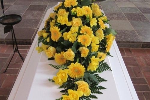 Kistepynt med solsikker og grønt løv på hvid kiste