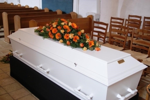 Kistepynt med gule og hvide blomster arrangeret på kiste i kirkerum