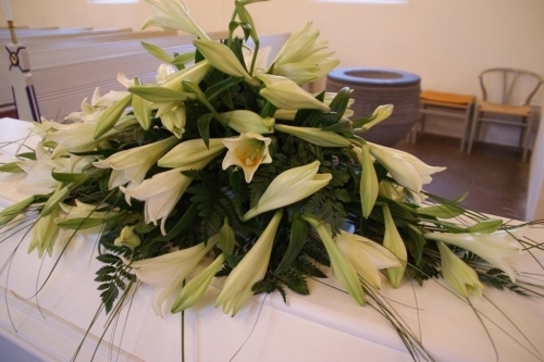 Kistepynt med orange blomster og hvidt mindebånd på kiste