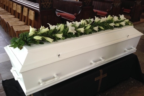 Kistepynt med røde roser og hvide blomster lagt på hvid kiste