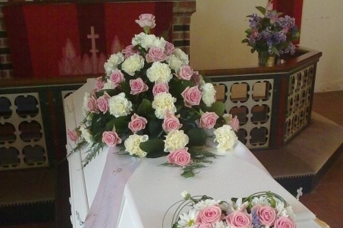 Kistepynt med lyserøde roser og hvide nelliker arrangeret på hvid kiste til begravelse