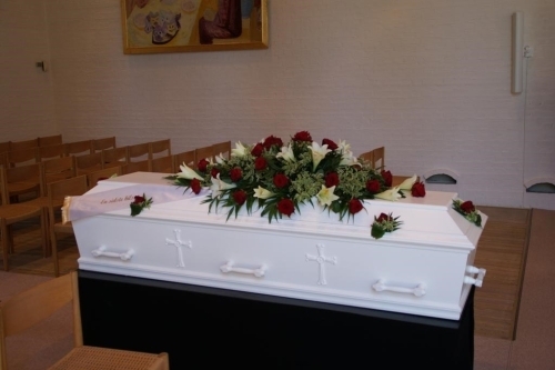 Klassisk kistepynt med røde og hvide roser arrangeret på hvid kiste