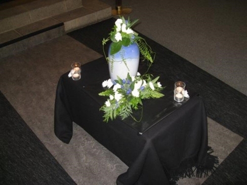 Urne med blå og hvide blomsterdekoration samt lys til bisættelse