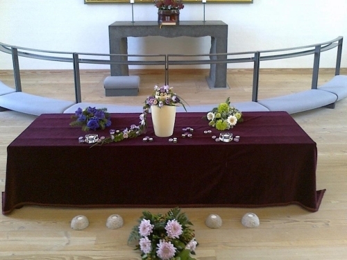 Urne med hvid blomst og grønne blade på lilla dug til mindehøjtidelighed