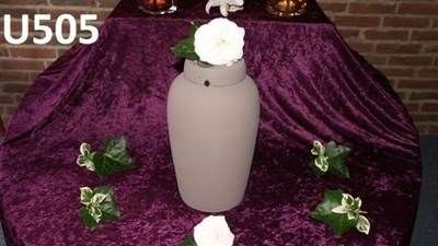 Urneopstilling med lilla drapering og blomster omkring urnen